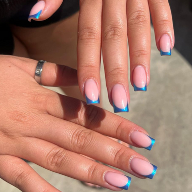 Close-up of hands with blue and pink nail design on a neutral background